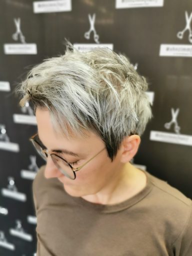 Person mit grauen Haaren und Brille, schaut nach unten, im Friseursalon.
